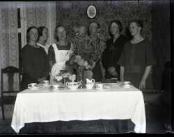 Fem kvinnor och en man med ett barn i famnen vid ett dukat bord. - klicka f�r att f�rstora