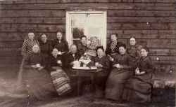En grupp kvinnor och ett barn framf�r en byggnad. Fr�n v�nster st�r Josefina Olsson i Knista by, Karolina Alexandersson i �sta, fosterdotter till urmakare Klinglund i �sta, Rakel Watz i Prostg�rden senare gift med pastor Johnsson i S�dert�lje (S�dertege?), fru Alda Gustafsson med dottern Astrid i Hidingebro, fr�ken Eva Hagberg i Edsbergs prostg�rd, fru Gerda Eriksson i V�sby i Kr�cklinge. Sittande syns Lars Olsmara i Knista by, fru klockare Larsson i Knista, fru Lovisa Klinglund gift med urmakare Klinglund, prostinnan Watz i Knista, fru Andersson i �sta som var mor till Professor Gunnar Andersson och fru Ester Larsson f�dd Watz gift med rektor Rob Karlsson - klicka f�r att f�rstora