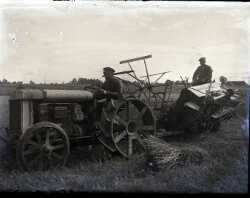 Två män på en traktor med järnhjul och en självbindare efter - klicka f�r att f�rstora