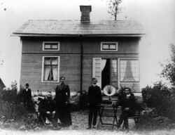 Familjen J A Berg framfr byggnad med Filip vid trdgrdsmblerna och Ernhard Berg vid trattgrammofonen - klicka fr att frstora